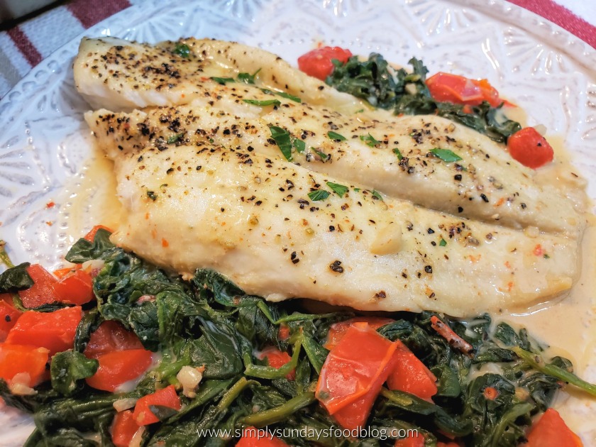 A fillet of flounder seasoned with salt, pepper and fresh parsley on a bed of spinach and red bell peppers with cream sauce